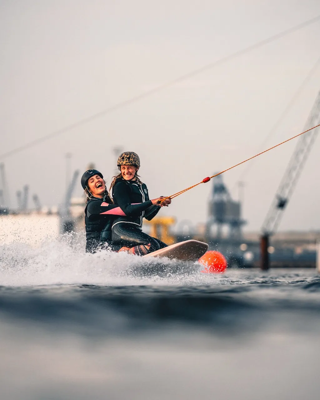 Zwei Frauen lachen gemeinsam bei einer Womens Wake Session auf dem Wasser